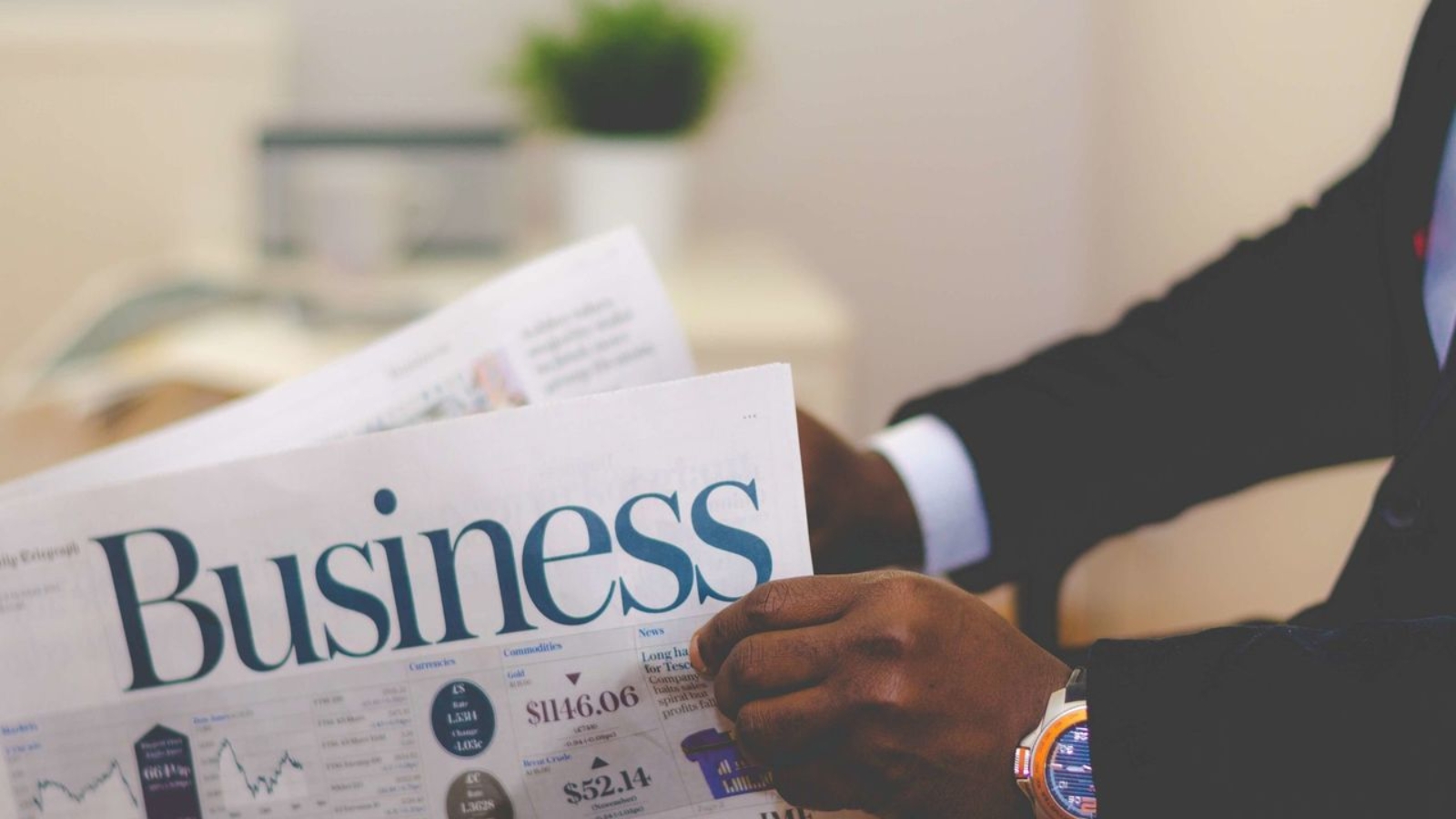 Close-up of a businessman reading a newspaper indoors, focusing on business headlines.